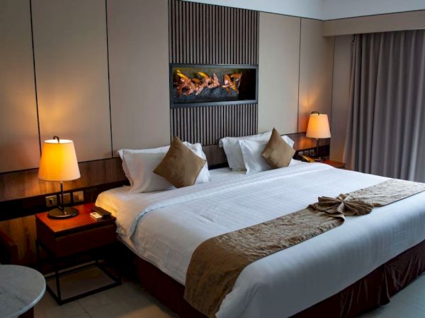 A cozy hotel room with a king-sized bed, side tables with lamps, wall art, neutral tones, and a well-lit atmosphere.