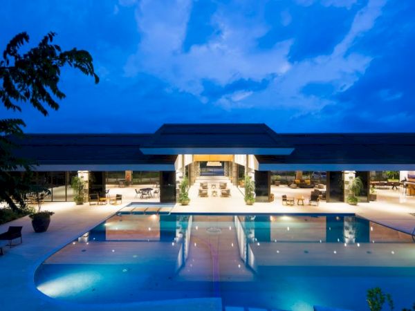 A luxurious outdoor pool area at night, featuring a large pool in front of a modern building with open spaces and seating areas.